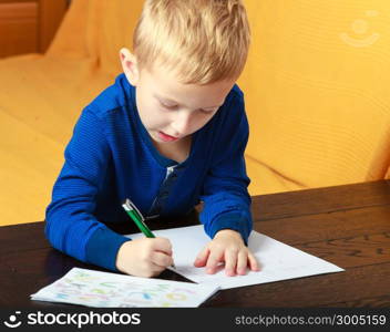 Happy childhood. Blond boy child kid with pen writing on piece of paper doing homework. At home.