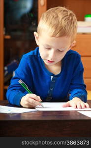 Happy childhood. Blond boy child kid with pen writing on piece of paper doing homework. At home.