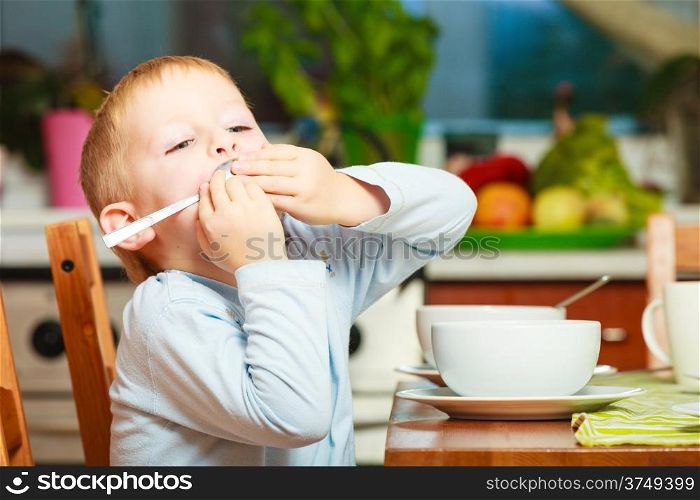 Happy childhood. Blond boy kid child eating corn flakes cereal with milk breakfast morning meal at the kitchen table. Home indoor
