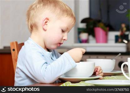 Happy childhood. Blond boy kid child eating corn flakes cereal with milk breakfast morning meal at the table. Home.