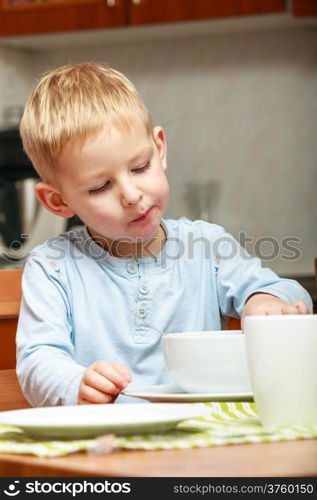 Happy childhood. Blond boy kid child eating corn flakes cereal with milk breakfast morning meal at the kitchen table. Home indoor