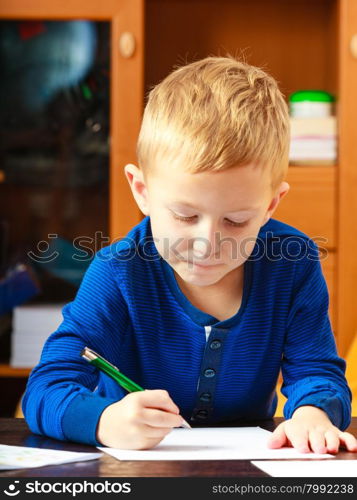 Happy childhood. Blonde boy child kid with pen writing drawing on paper doing homework. At home.