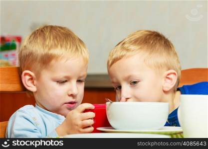 Happy childhood. Boys kids children eating corn flakes cereal with milk breakfast morning meal. Brothers playing with mobile phone at the table. Home.