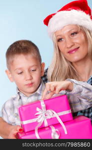 Happy childhood, holidays christmas time. Mother in santa claus hat and little boy child with stack of pink presents gift boxes on blue