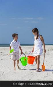 Happy children, boy girl, brother and sister having fun walking and playing in the sand on a beach with bucket and spade