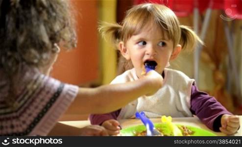 Happy children having fun at lunch, female child helping her friend during meal with pasta at school
