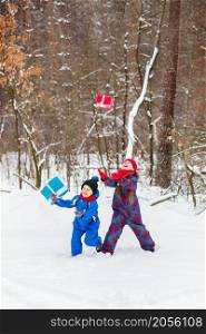 Happy children in a winter snow-covered forest with gift boxes. Christmas fun for Christmas and New Year.. Happy children in a winter snow-covered forest with gift boxes.