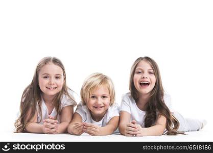 Happy children isolated on white. Happy smiling three children in white clothes laying on floor isolated on white background