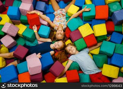 Happy children lying in soft cubes, playground in entertainment center. Play area indoors, play room. Happy children lying in soft cubes, playroom