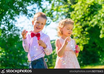 Happy children play with soap bubbles on the lawn