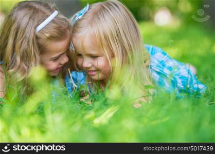Happy children relaxing on green grass in summer park and talking. Healthy lifestyles concept.