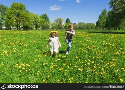 Happy children run on meadow. Happy children friends run and play outdoors on yellow dandelion flower meadow