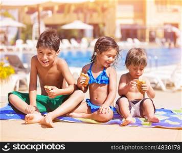 Happy children sitting near the pool and eating croissants, having break after swimming, two cheerful brother and cute sister enjoying summer vacation on beach resort