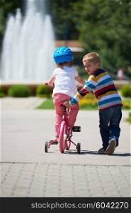 Happy childrens outdoor, brother and sister in park have fun. Boy and girl in park learning to ride a bike.