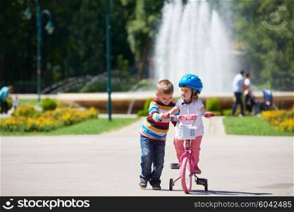 Happy childrens outdoor, brother and sister in park have fun. Boy and girl in park learning to ride a bike.