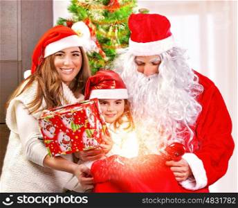 Happy Christmas celebration, cheerful parents give festive gift to adorable sweet child, wearing Santa Claus costume, New Year party concept