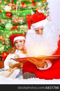 Happy Christmas eve at home, cute little baby girl sitting near beautiful xmas tree and reading magic book with Santa Claus, enjoying winter holidays