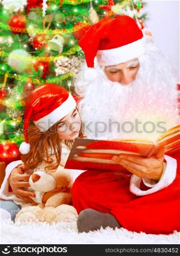 Happy Christmas eve at home, cute little girl sitting near beautiful xmas tree and reading magic book with Santa Claus, enjoying winter holidays concept