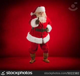 Happy Christmas Santa Claus showing thumb up. Red background. Full length