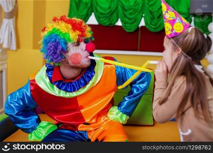 Happy clown and little girl plays with tube on birthday party.