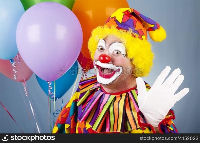 Happy clown with helium balloons, waving hello.