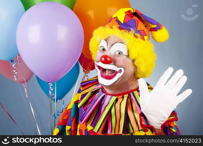 Happy clown with helium balloons, waving hello.