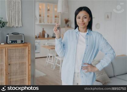 Happy confident arab woman holding house keychain in hand. Real estate purchase celebrating. Mortgage loan and investment concept. Relocation and housing. Modern scandinavian interior of apartment.. Happy confident woman is holding house keychain in her hand. Real estate purchase celebrating.