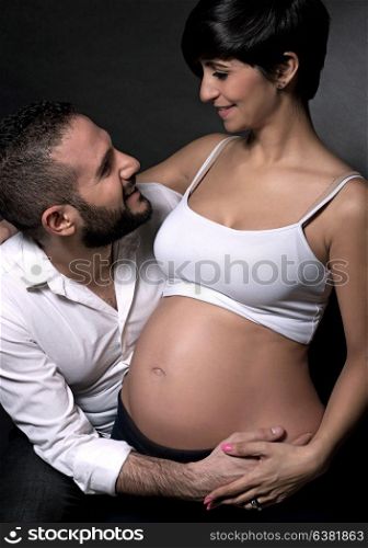 Happy couple awaiting baby, beautiful pregnant woman with handsome husband over black background, enjoying parenthood