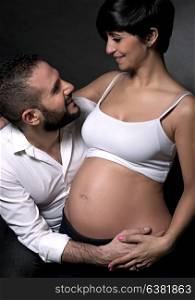 Happy couple awaiting baby, beautiful pregnant woman with handsome husband over black background, enjoying parenthood