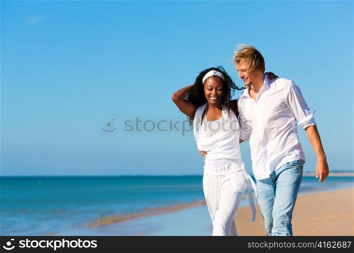 Happy couple - black woman and Caucasian man - walking and running down a beach in their vacation