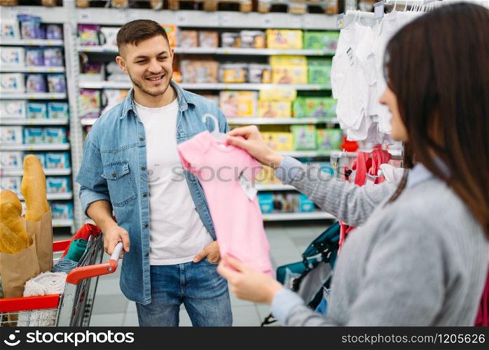 Happy couple buying childrens clothes in a supermarket, family shopping. Customers in shop, buyers in market, department of goods for kids
