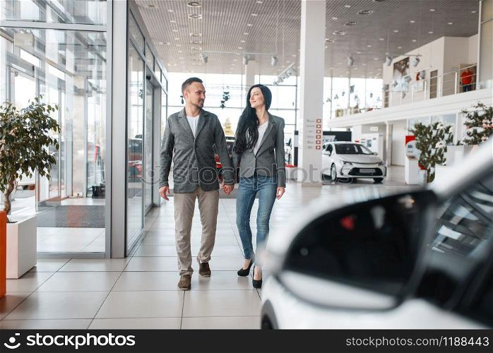 Happy couple buying new car in showroom. Male and female customers choosing vehicle in dealership, automobile sale, auto purchase. Happy couple buying new car in showroom