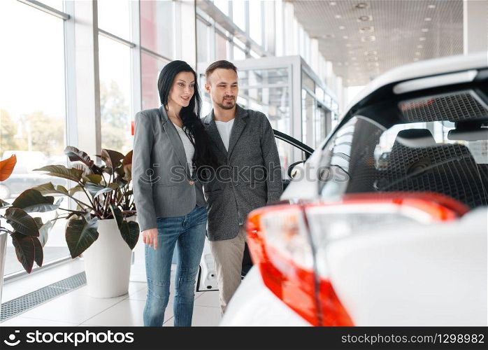 Happy couple buying new car in showroom. Male and female customers choosing vehicle in dealership, automobile sale, auto purchase. Happy couple buying new car in showroom