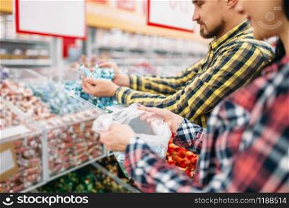 Happy couple buying sweets and candies in supermarket. Male and female customers on family shopping. Man and woman purchasing food. Couple buying sweets and candies in supermarket