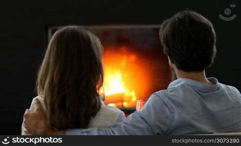 Happy couple clinking red wine glasses near fireplace