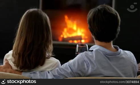 Happy couple clinking red wine glasses near fireplace