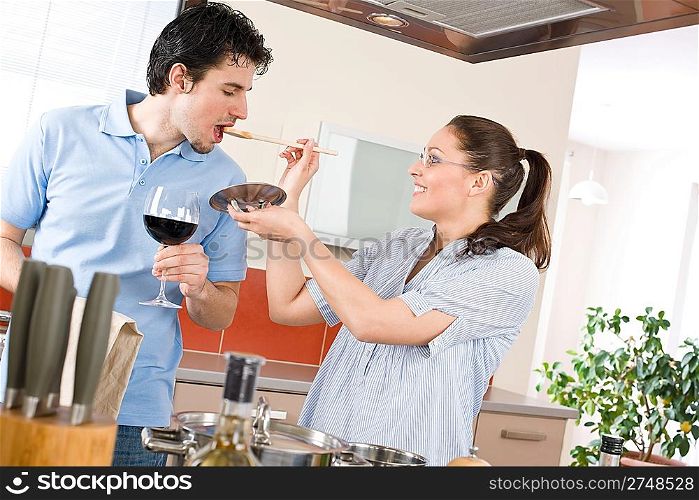 Happy couple cook together in modern kitchen tasting food, drink red wine