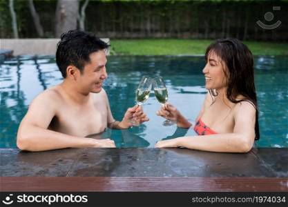 happy couple drinking champagne glass at the edge of swimming pool