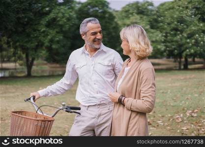 Happy couple elderly relaxing at park walking with bike and talking together in morning time. The concept of good health and relax