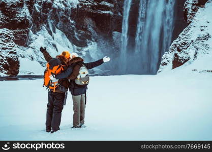 Happy couple enjoying amazing view on Skogafoss waterfall, having fun in winter travel to Iceland, active wintertime honeymoon