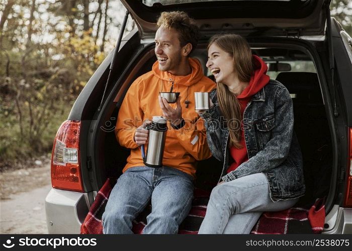 happy couple enjoying hot beverage trunk car