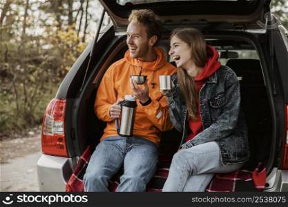 happy couple enjoying hot beverage trunk car