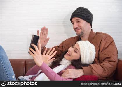 Happy couple greeting in a phone video call while relaxing on sofa in living room at home