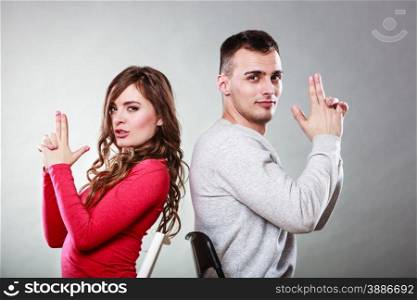 Happy couple having fun and fooling around pretending their hands fingers are guns. Joyful man and woman have nice time sitting back to back. Good relationship.. Couple having fun pretend hands fingers are guns.
