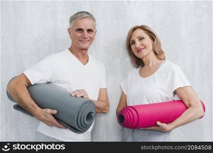 happy couple holding leaning white wall holding rolled yoga mat