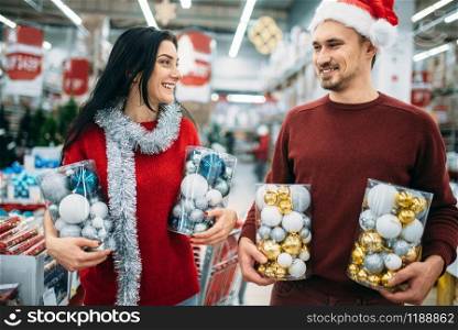 Happy couple holds boxes with Christmas toys in shop, family tradition. December shopping of holiday goods and decorations. Happy couple holds boxes with Christmas toys