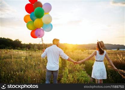 Happy couple holds bunch of balloons and kissing in wheat field. Pretty couple leisure on summer meadow. Couple holds balloons and kissing in wheat field