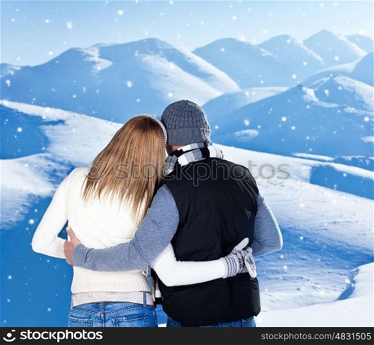 Happy couple hugging outdoor at winter mountains, rear view, two in love over natural blue wintertime landscape background with falling snow, romantic Christmas vacation holidays