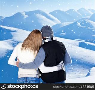 Happy couple hugging outdoor at winter mountains, rear view, two in love over natural blue wintertime landscape background with falling snow, romantic Christmas vacation holidays