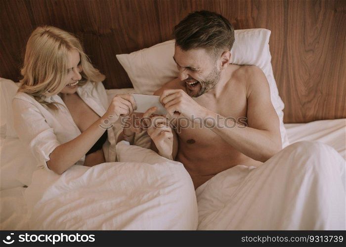 Happy couple in bed at home and use mobile phone
